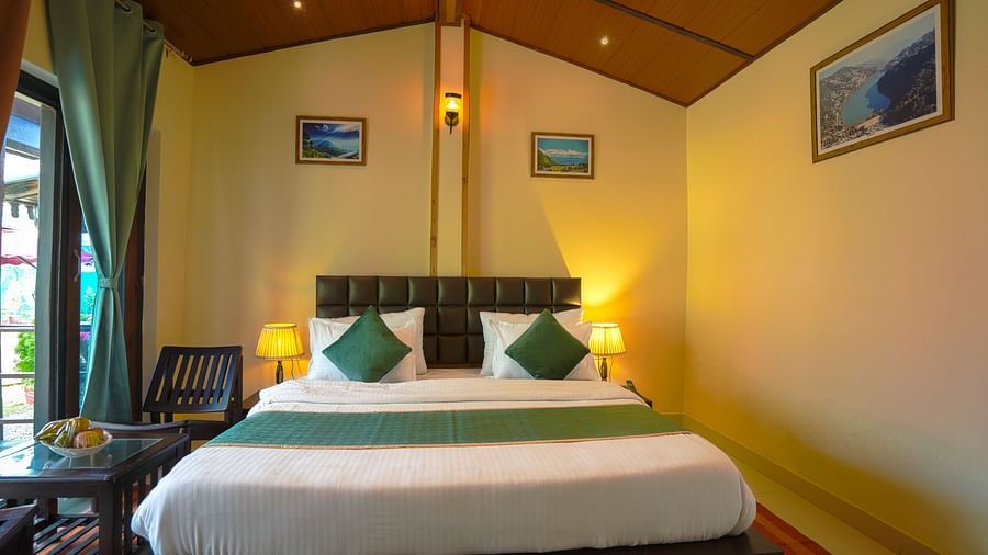 A lightfilled room with a bed, 2 chairs and wall paintings arranged in a proportionate manner
